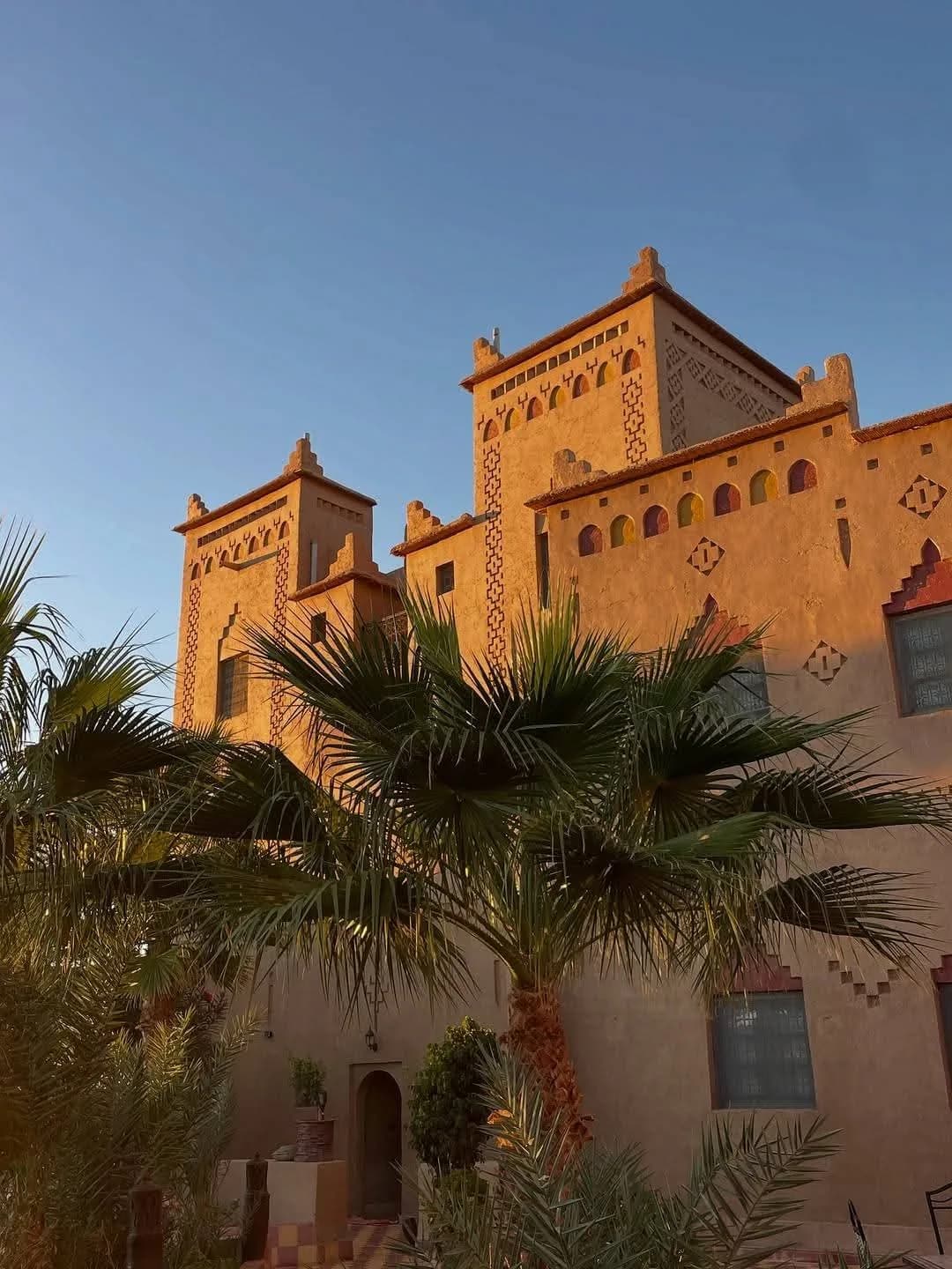 Kasbah de terre ocre entourée de palmiers sous un ciel clair
