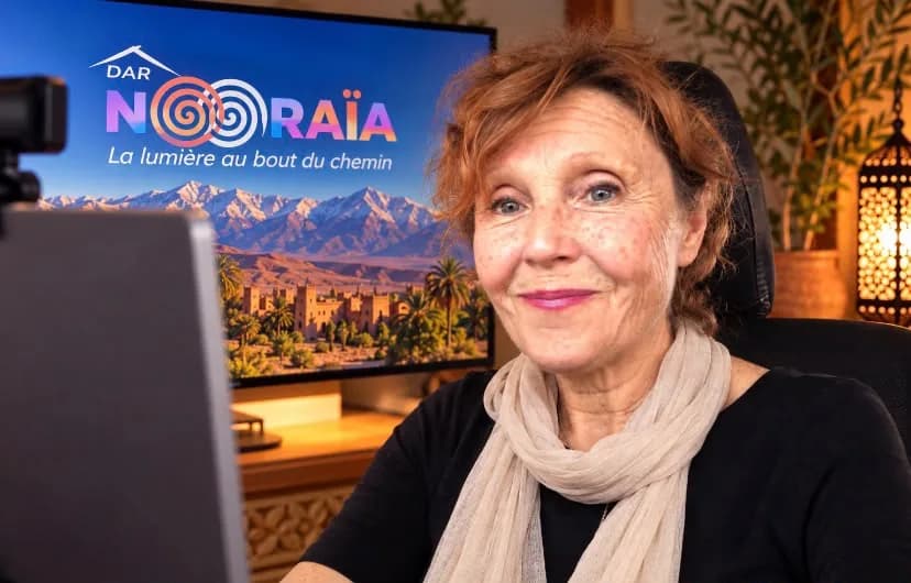 Dominique, souriante, installée devant son ordinateur pour un petit salon en direct, l’écran affichant Dar Nouraïa et l’Atlas