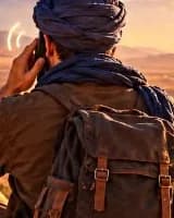 Un voyageur au turban bleu, sac au dos, téléphone à l’oreille face aux montagnes du Sud marocain