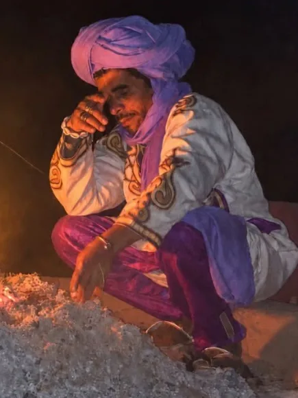 Mohammed, en turban violet, accroupi près d’un feu de camp dans le désert