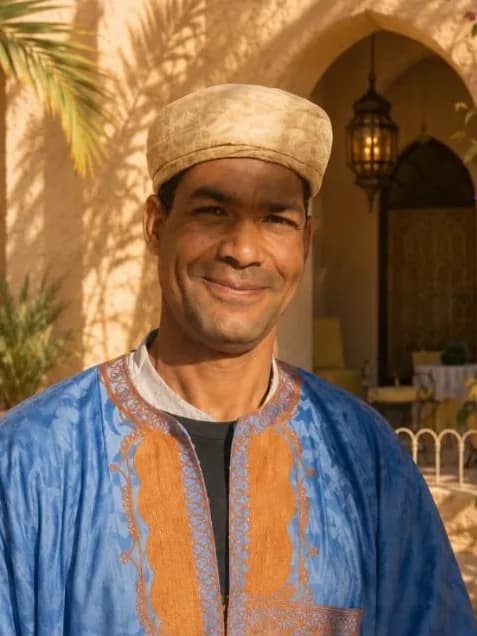Mustapha, souriant en djellaba bleue brodée, dans le patio fleuri d’un riad