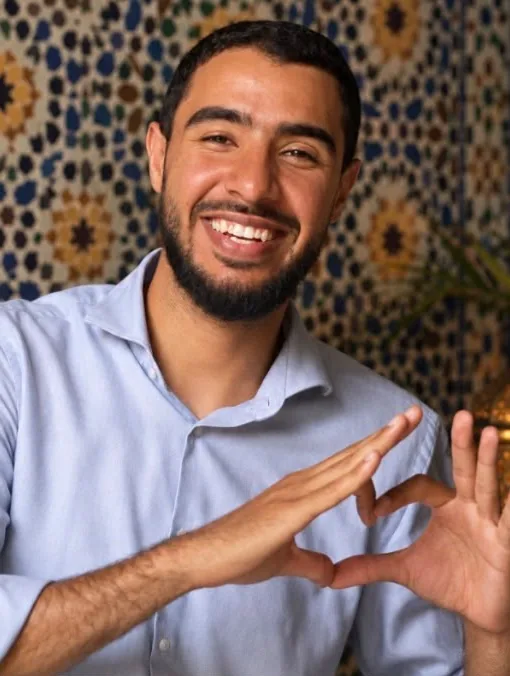 Rachid, tout sourire, formant un cœur avec ses mains devant un mur de zellige
